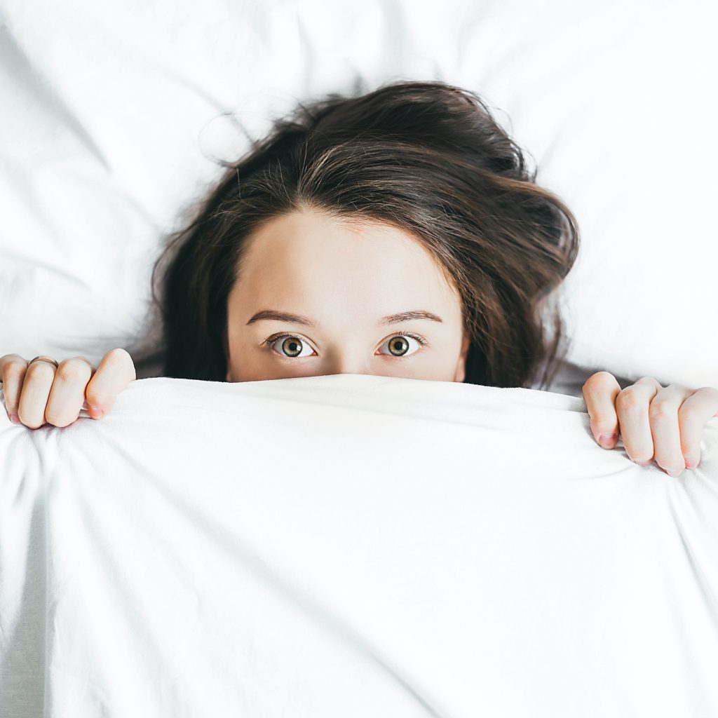 Photo by Alexandra Gorn on Unsplash A girl with brown hair pulling up white sheets to her face. Here is 10 ways to ease period cramps.