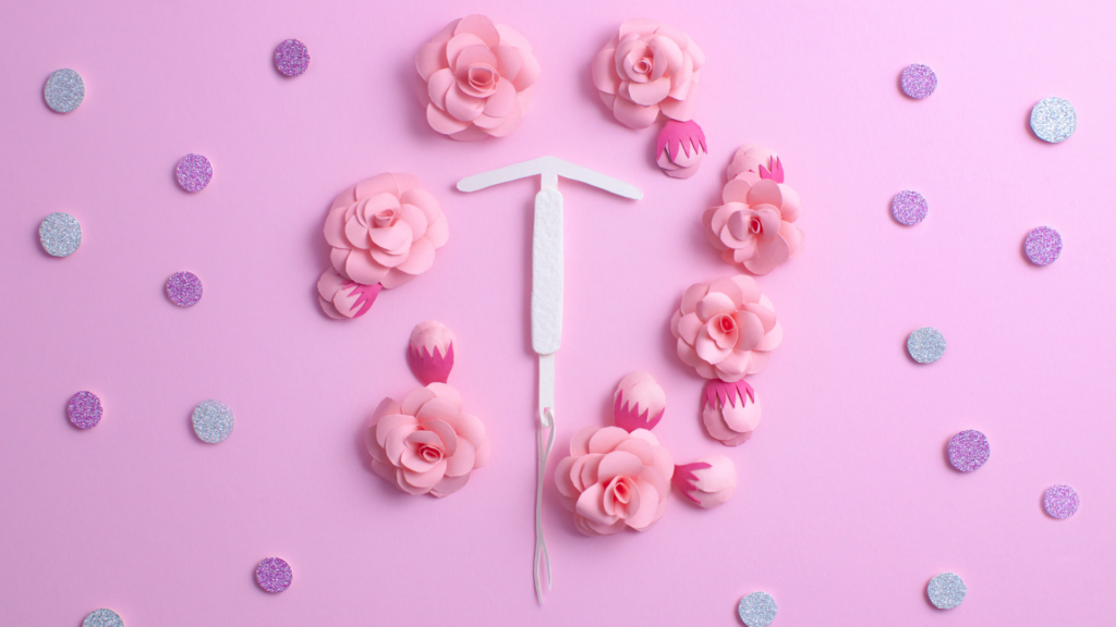 How IUDs Influence Your period. White cardboard iud surrounded by pink flowers on a pink background.