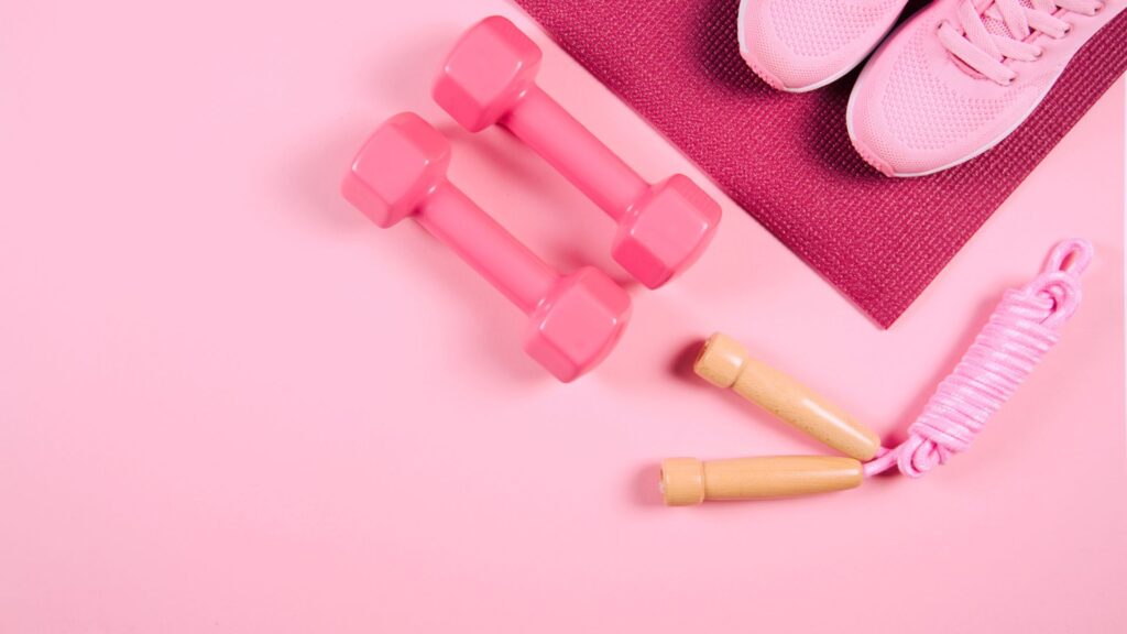 Pink dumbbells and jumprope next to a pair of pink sneakers on a pink yoga mat