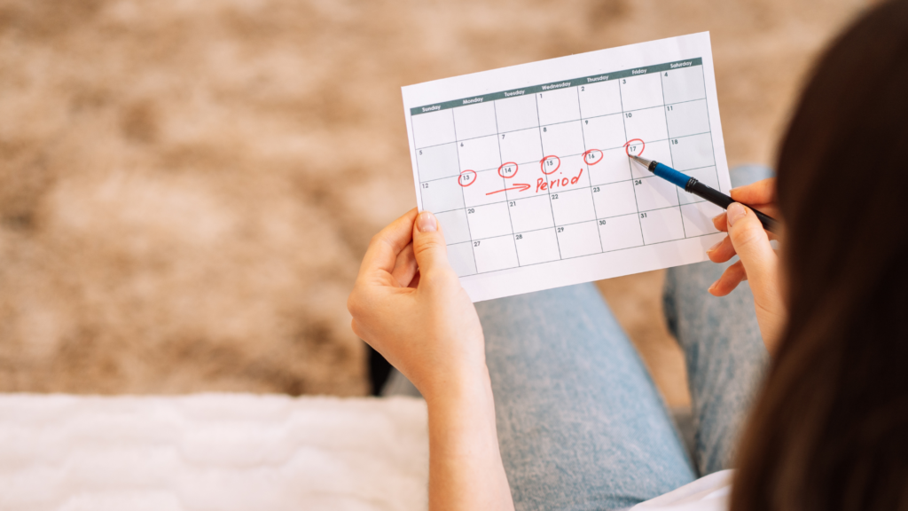 Woman looking at a calendar with 5 dates circled in red and the word "period" written along those days