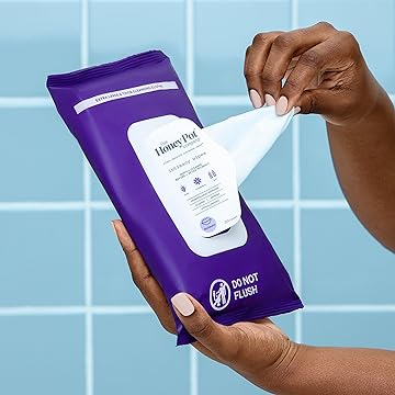 Hands pulling a wipe out of a purple package of The Honey Pot Company Intimacy Cleansing Wipes