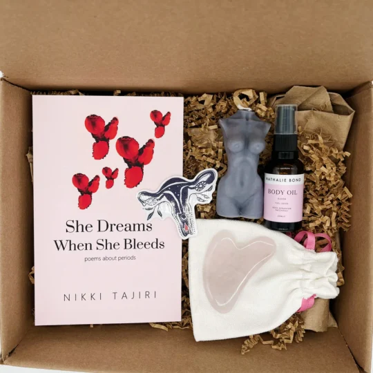 Box filled with items from the I Am Divine Period Care Package from My Club Red including poetry book, uterus sticker, rose quartz gun she stone, goddess candle, body oil and womb connection guided meditation