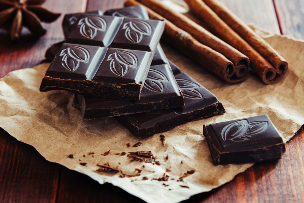 A stack of dark chocolate squares with a leaf design on top of each one. The chocolate is on top of some brown paper and there are cinnamon sticks in the background. Chocolate has long been thought of as an aphrodisiac or a libido boosting food. 