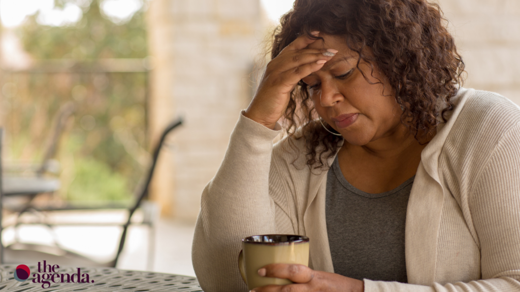 Middle aged black woman holding her head in one hand and her coffee in the other
